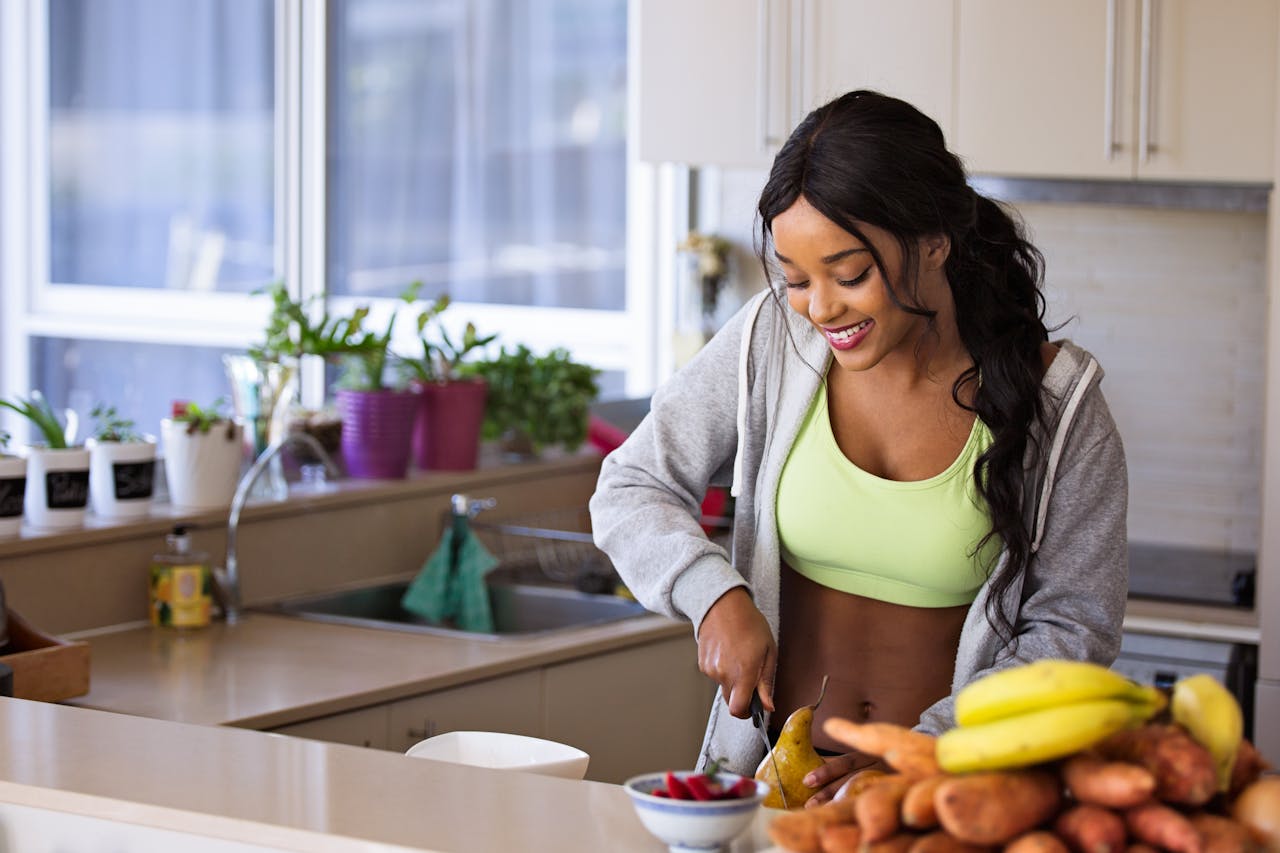 heros-img Smiling woman preparing fresh fruit in a sunlit kitchen, embodying a healthy lifestyle.